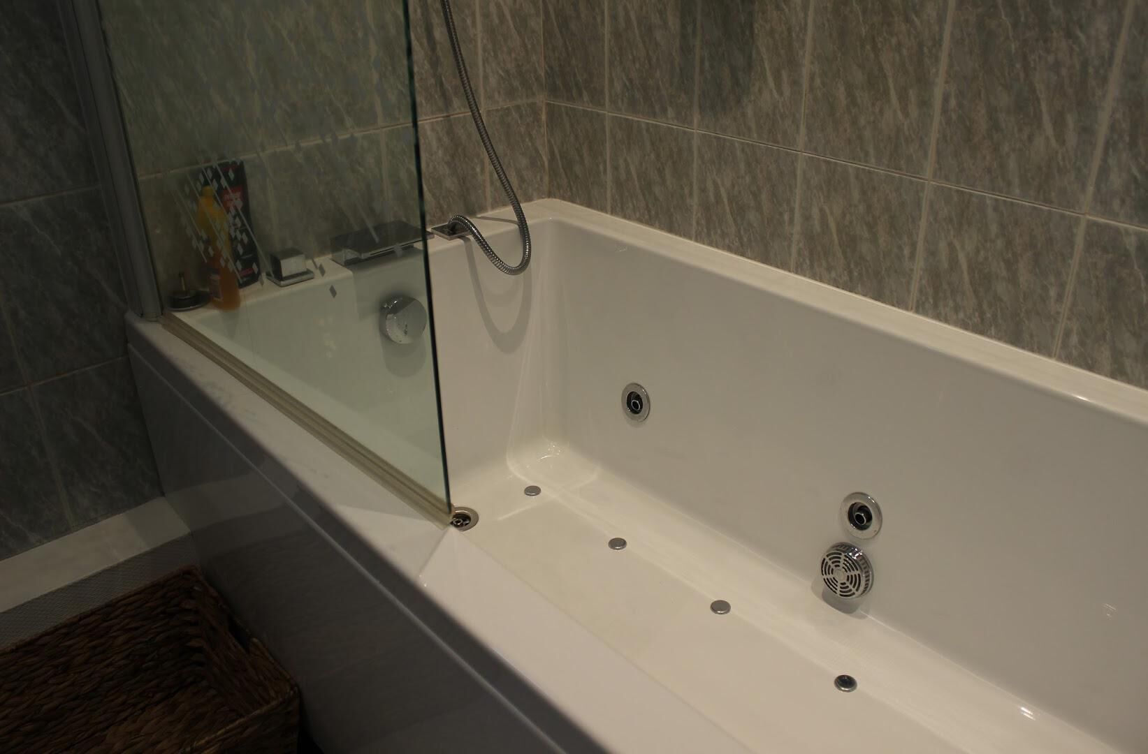 Ein modernes Badezimmer mit einer Glaskabinentubus, Marmorwänden und einem Korbwäscheschrank.