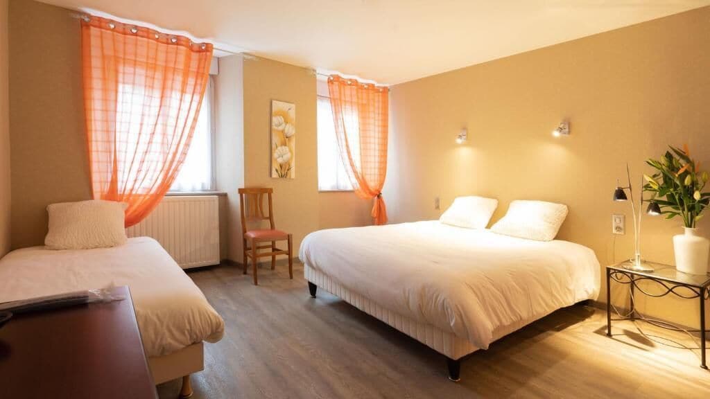 Una habitación de hotel con dos camas, una silla, una mesa y una planta.