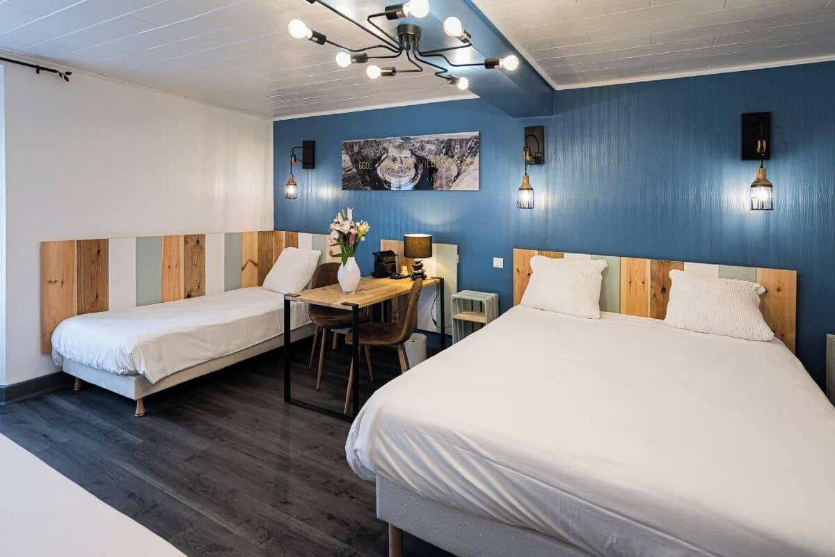 A room with two beds, a wooden desk, a chair, and a table.