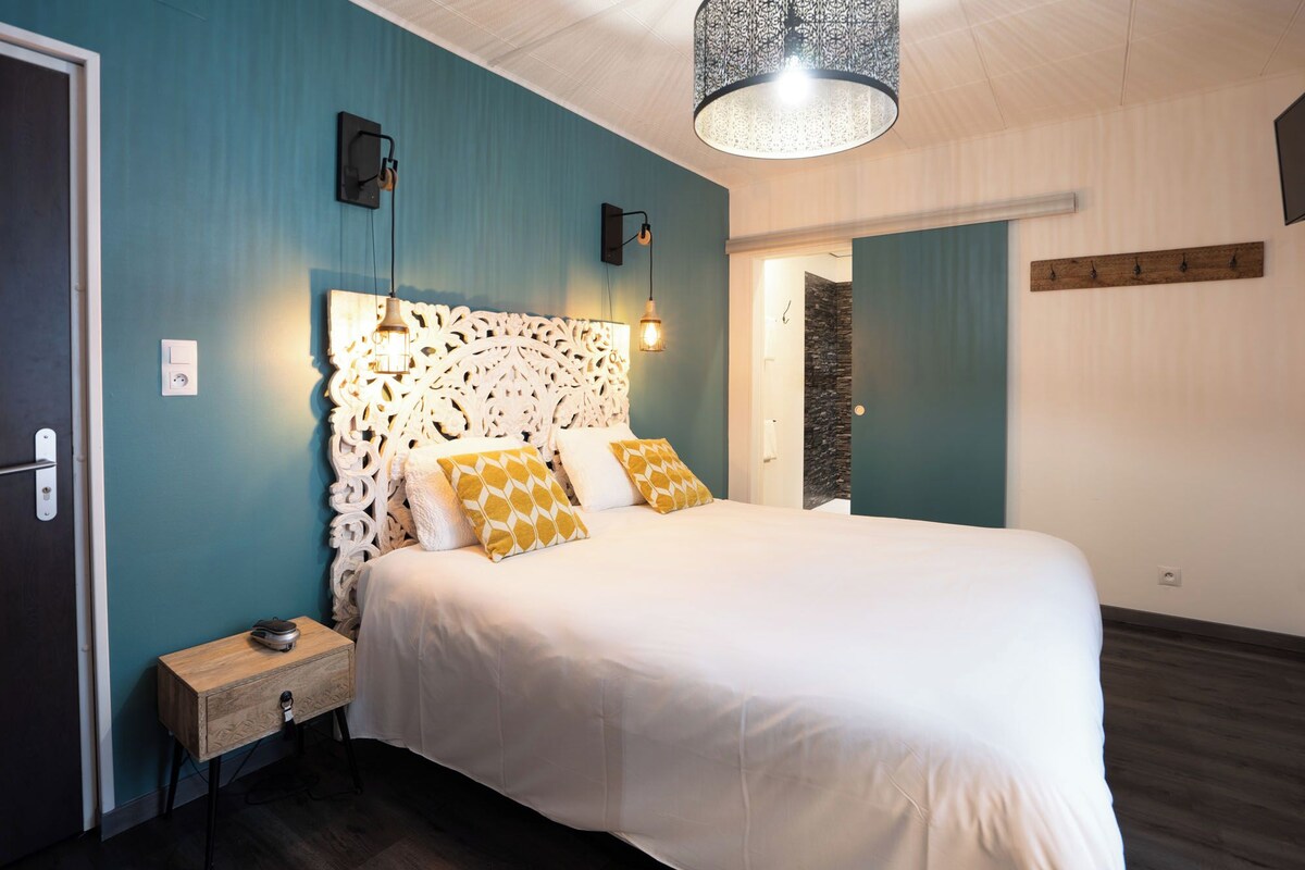 A bedroom with a white bed, teal walls, a decorative headboard, and a hanging light fixture.