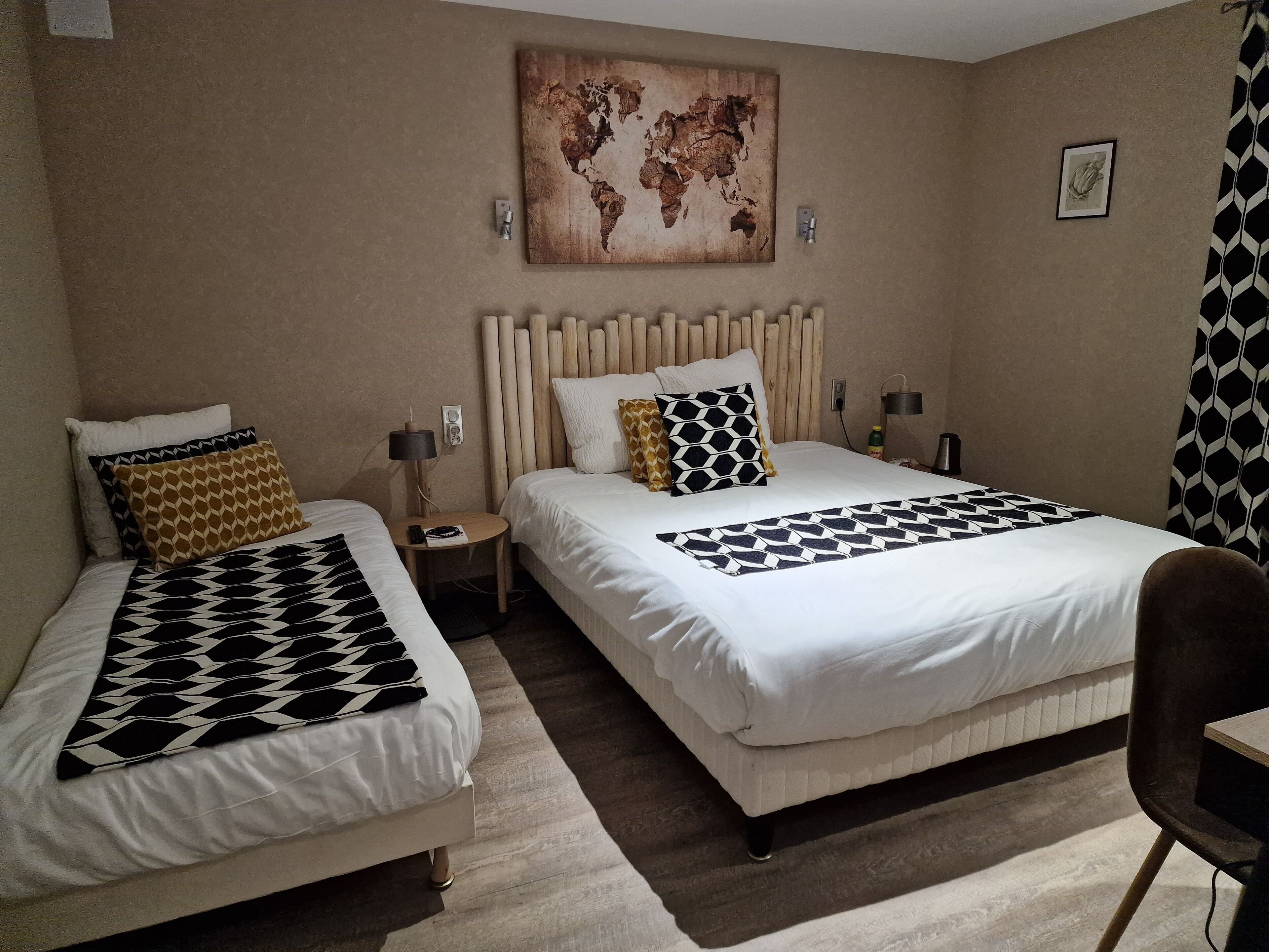 Habitación de hotel con dos camas, un mapa mundial en la pared, una mesita con lámpara y una silla.
