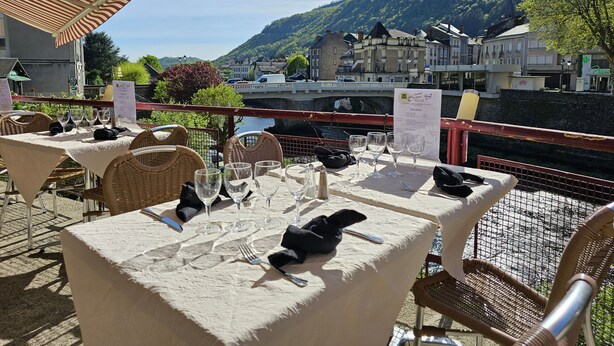 An outdoor dining area with tables set for two, overlooking a river and a bridge. - Logis Central Hôtel & Spa (Bort-les-Orgues)