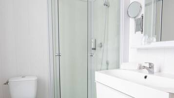 Un baño con ducha de vidrio, inodoro y lavamanos con espejo.