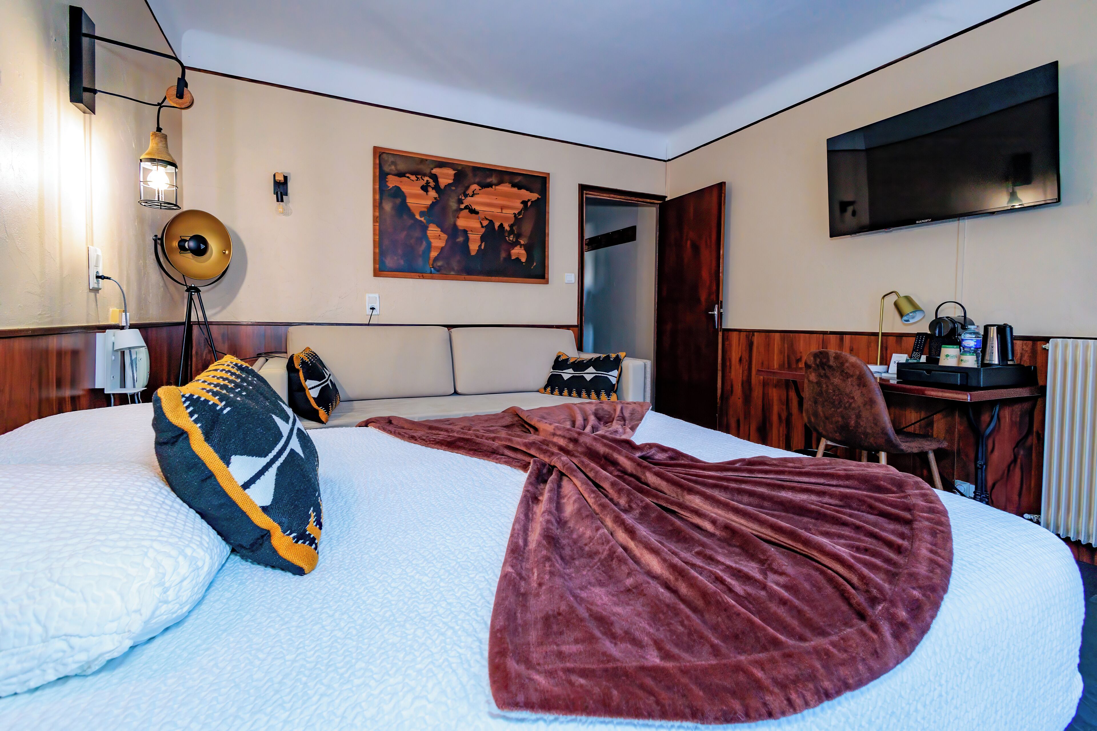 A hotel room with a large bed, a world map artwork, a TV, and a desk with a chair.