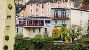 A hotel with a bar and restaurant on the ground floor, a balcony with red railings, and a view of a river. - Logis Central Hôtel & Spa (Bort-les-Orgues)