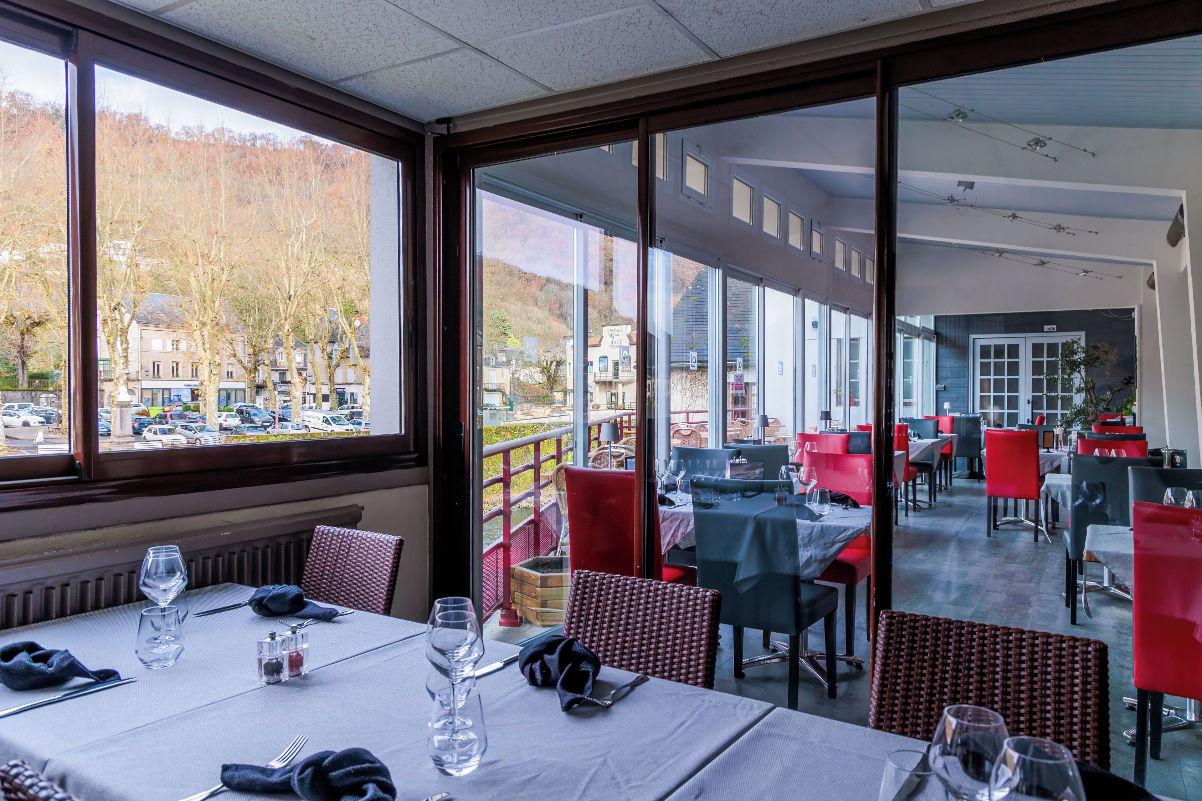 Ein Restaurant mit gedeckten Tischen, großen Fenstern mit Blick auf die Straße und Bäume, und einem modernen Innenraum.
