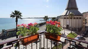 Een balkon met bloempotten met uitzicht op een kustplaatsje, met een opvallende kerktoren.