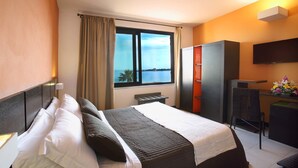 Een hotelkamer met een bed, een bureau, een stoel, een televisie en een raam met uitzicht op zee.