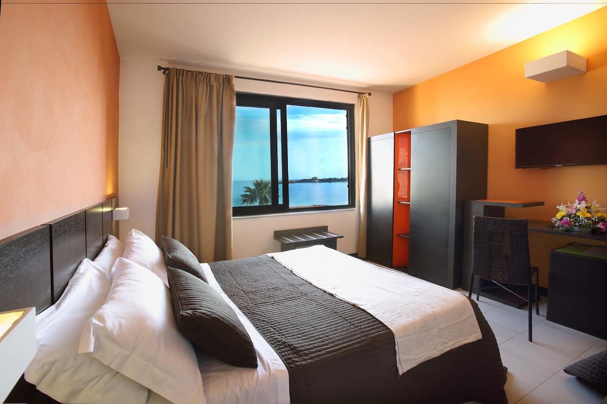 Une chambre d’hôtel équipée d’un lit, d’un bureau, d’une chaise, d’une télévision et d’une fenêtre donnant sur la mer.