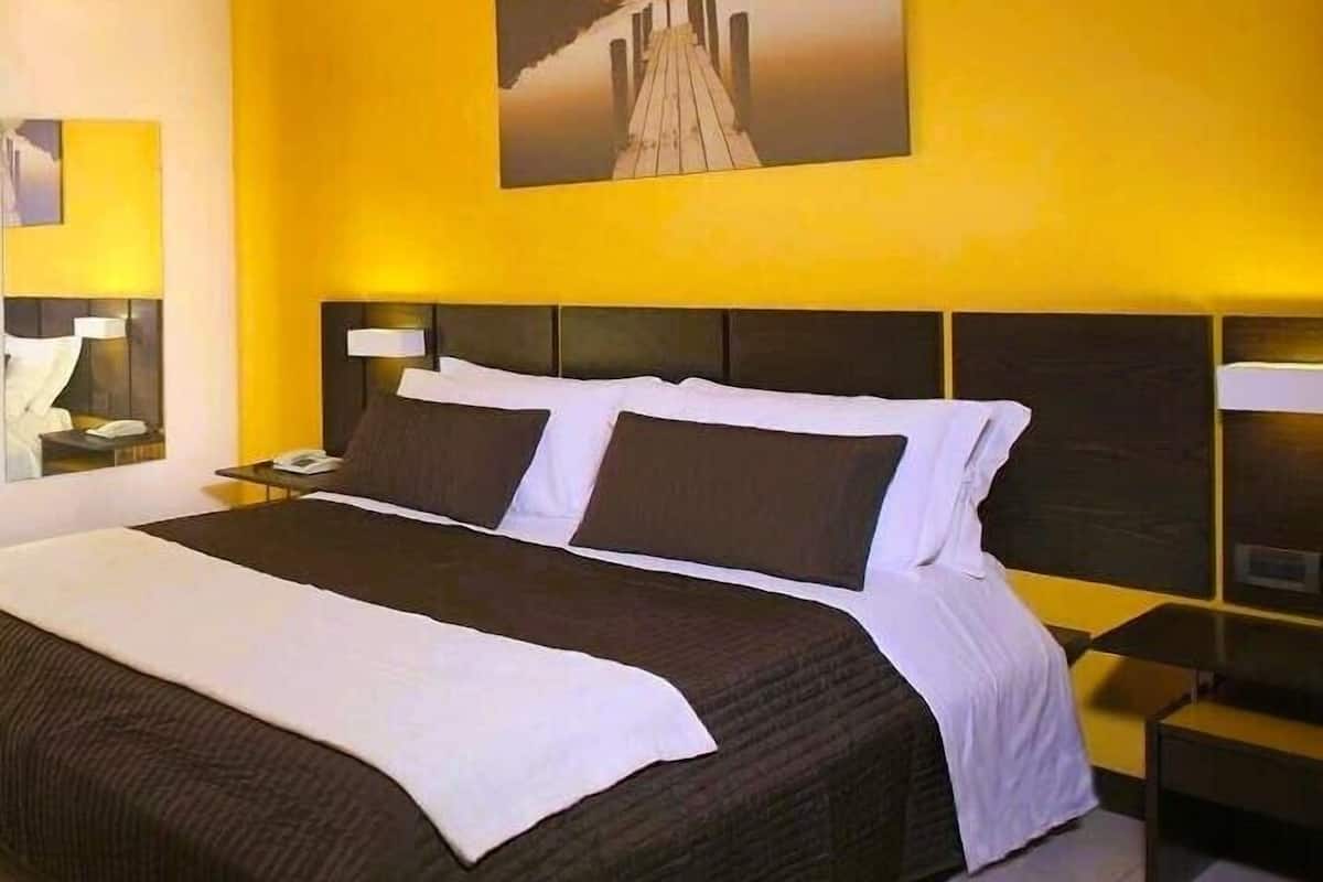 Une chambre d’hôtel avec un grand lit, une table de chevet, une lampe et un tableau au mur.