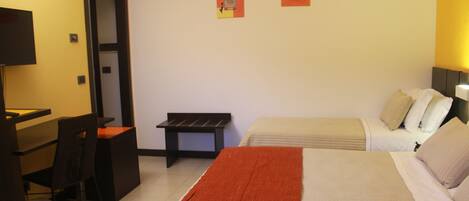 A hotel room with a bed, a desk, a chair, and two paintings on the wall.