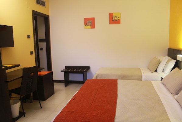 A hotel room with a bed, a desk, a chair, and two paintings on the wall.
