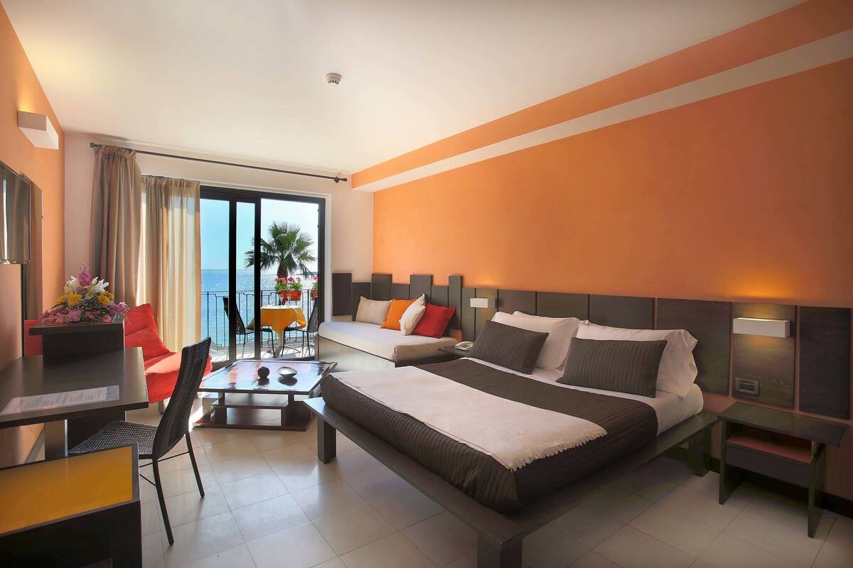 Une chambre d’hôtel avec deux lits, une table à manger et vue sur la mer.