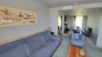 Una sala moderna con un sofá gris, una mesa de centro de madera y una zona de comedor con una mesa y sillas. Se ve una obra de arte grande en la pared.