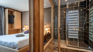 A modern hotel room with a wooden bed, a walk-in shower, and a wardrobe with hanging clothes.