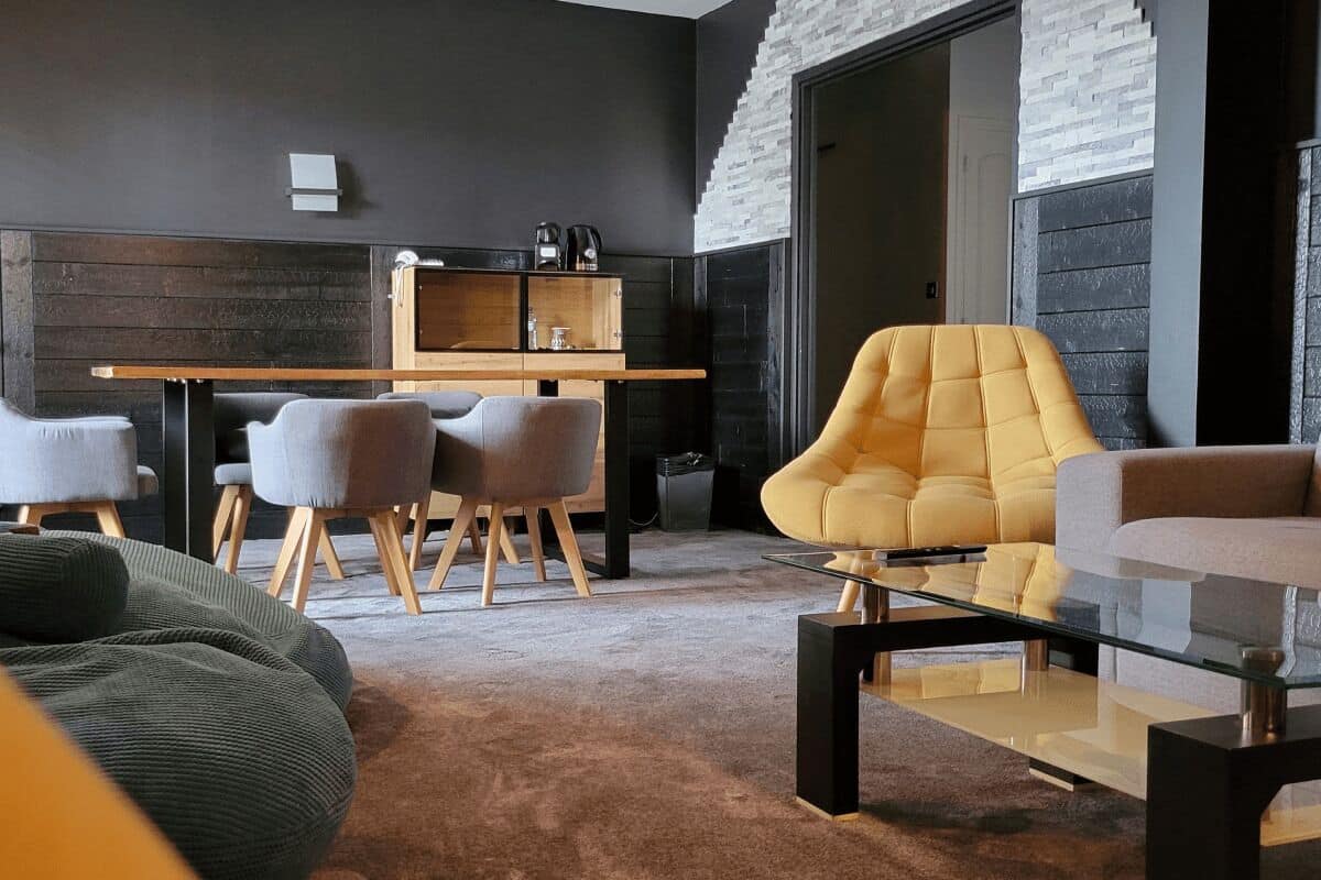 Uma sala de estar moderna com sofá, poltronas, mesa de centro de vidro e área de jantar com mesa e cadeiras de madeira.