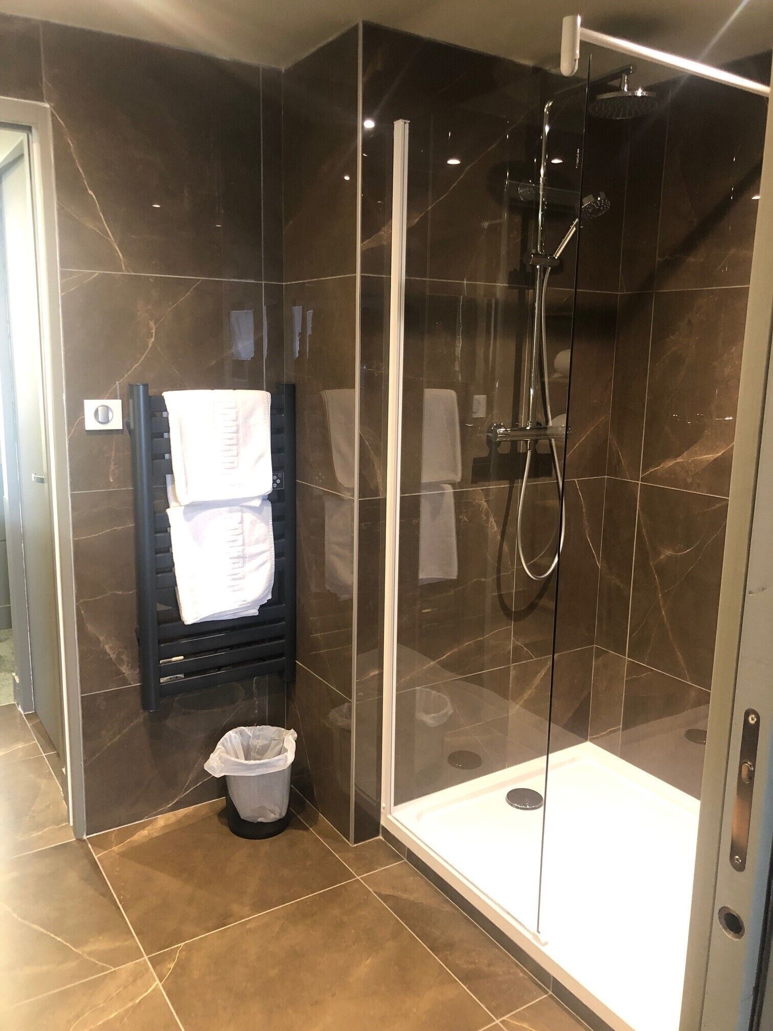 Un baño moderno con ducha envuelta en vidrio, un perchero con toallas y un cesto de basura.