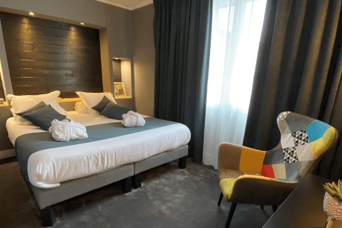 Quarto de hotel com uma cama grande, uma cadeira e uma mesinha com uma planta.