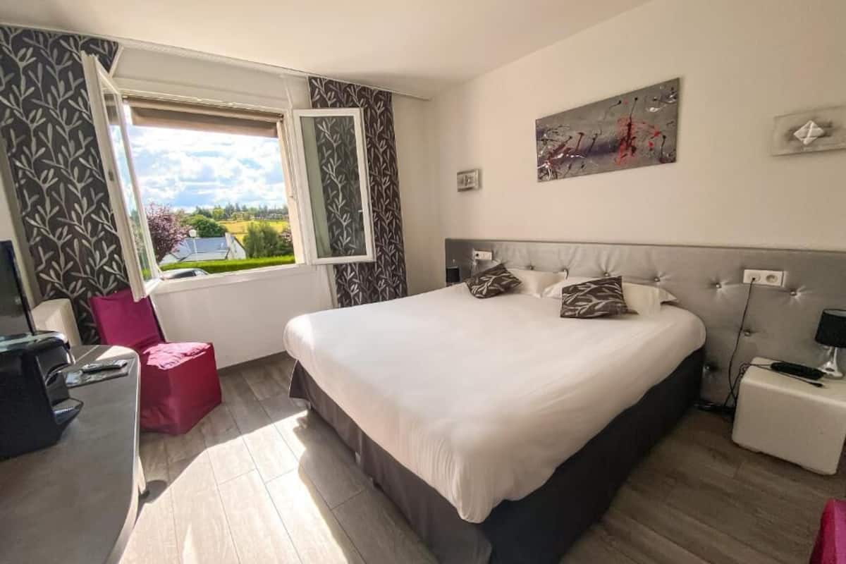 Quarto com uma cama grande, uma mesa de trabalho, uma cadeira, janela com vista e um quadro na parede.