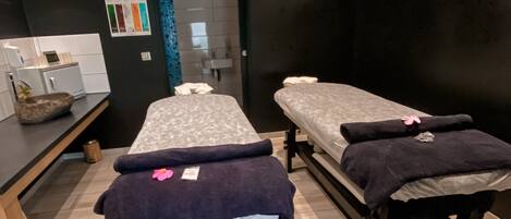 A spa room with two treatment beds, a sink, and a small counter with a decorative bowl.