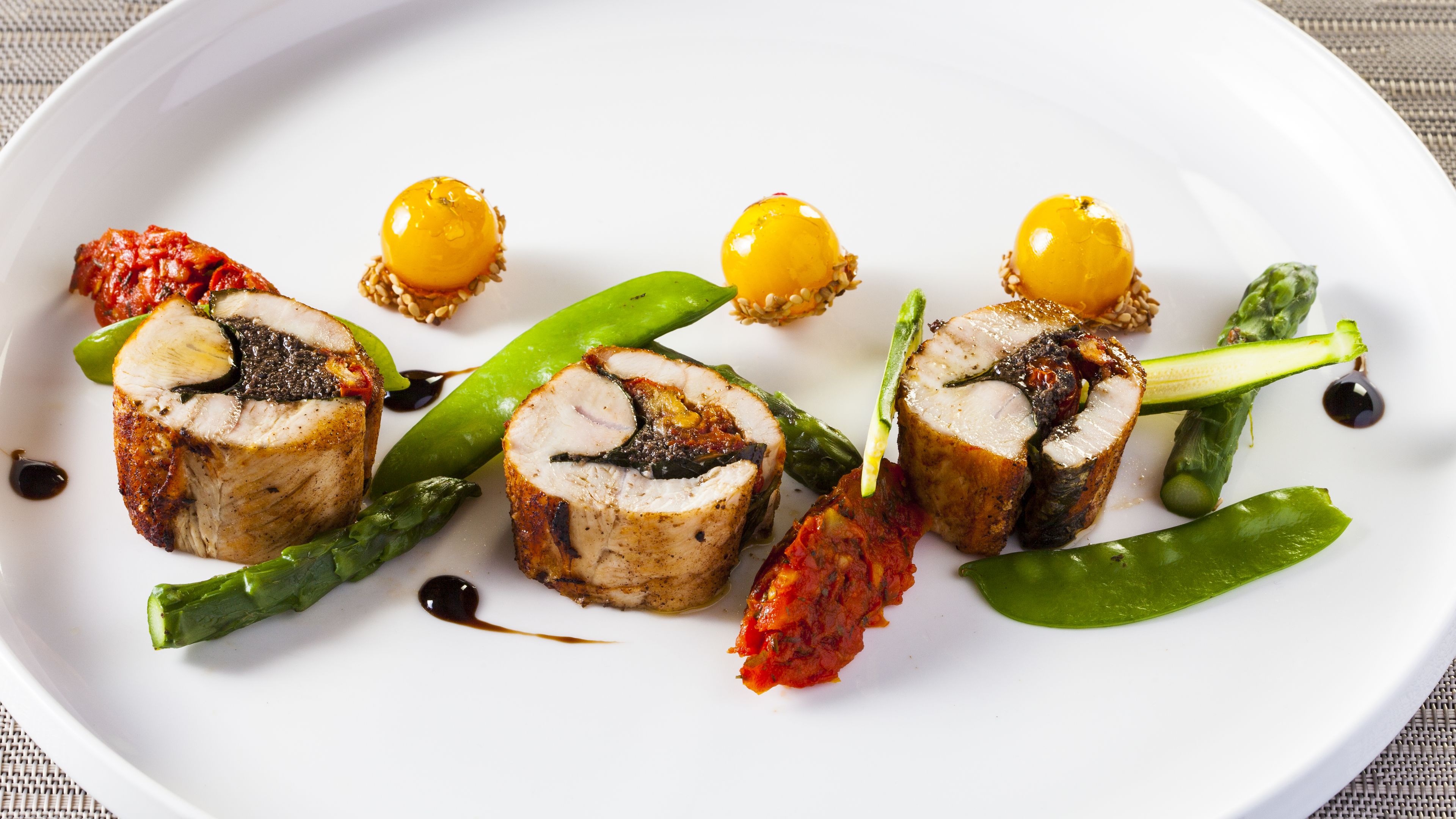 Une assiette blanche contenant un plat de viande hachée en forme de rouleau, des légumes verts et deux boules jaunes.