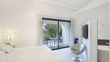 Une chambre d’hôtel moderne équipée d’un lit, d’un téléviseur fixé au mur, d’un balcon avec une table et des chaises, et d’une salle de bain avec une baignoire.