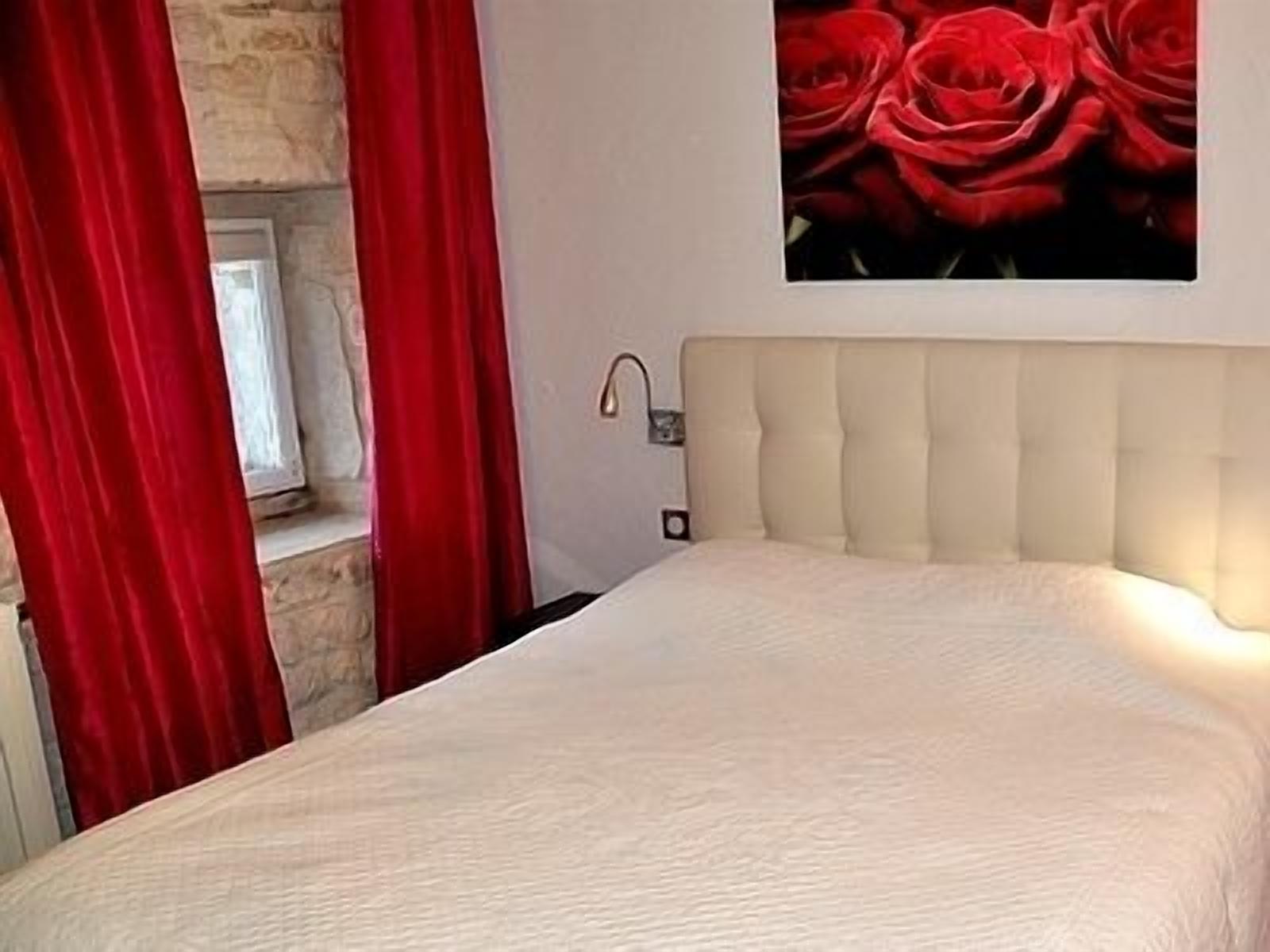 Une chambre à coucher avec un lit, une tête de lit, une fenêtre et un tableau représentant des roses rouges accroché au mur.