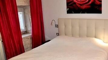 Une chambre à coucher avec un lit, une tête de lit, une fenêtre et un tableau représentant des roses rouges accroché au mur.