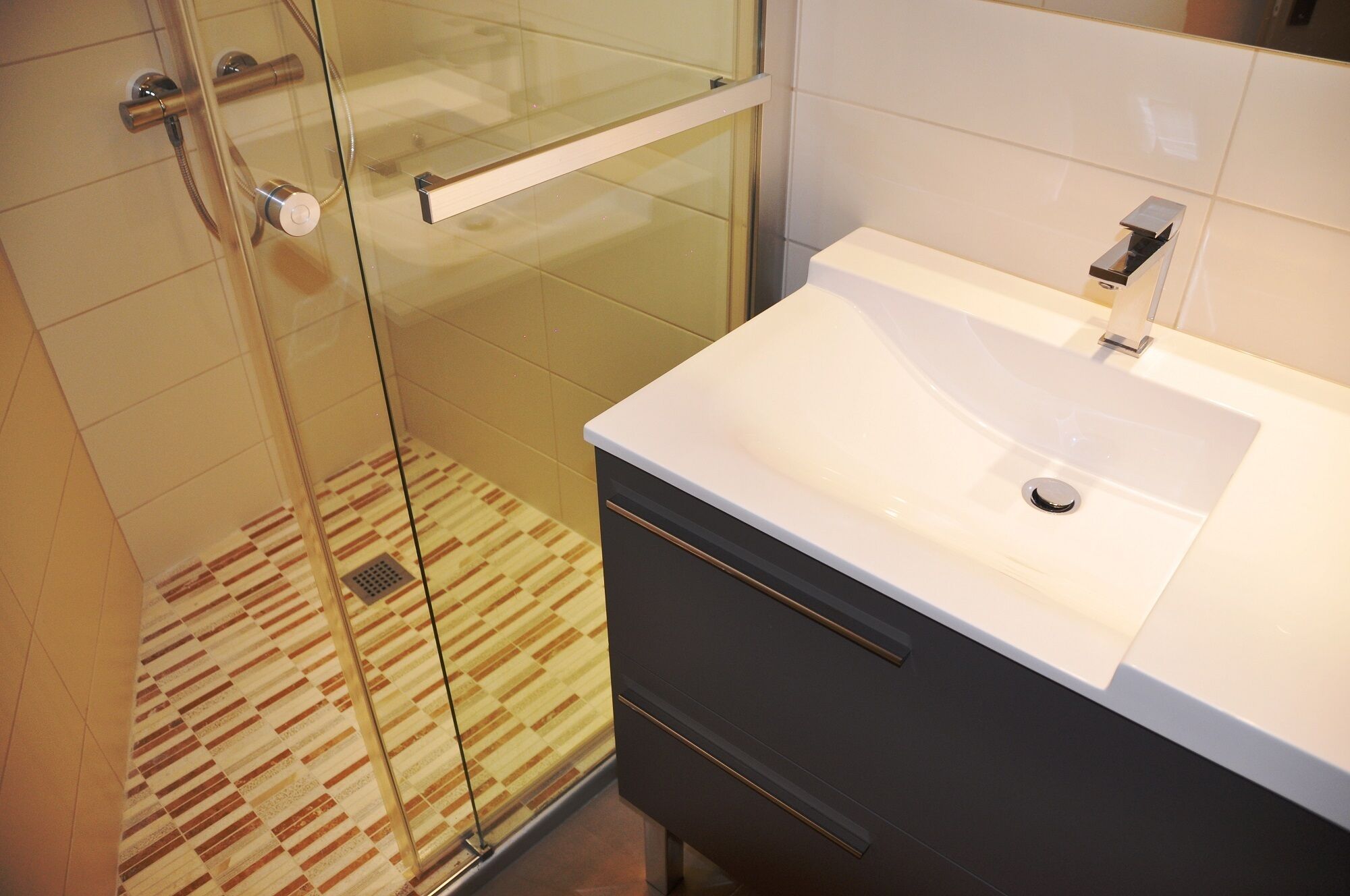 A modern bathroom with a glass shower enclosure, a white sink, and dark cabinetry.