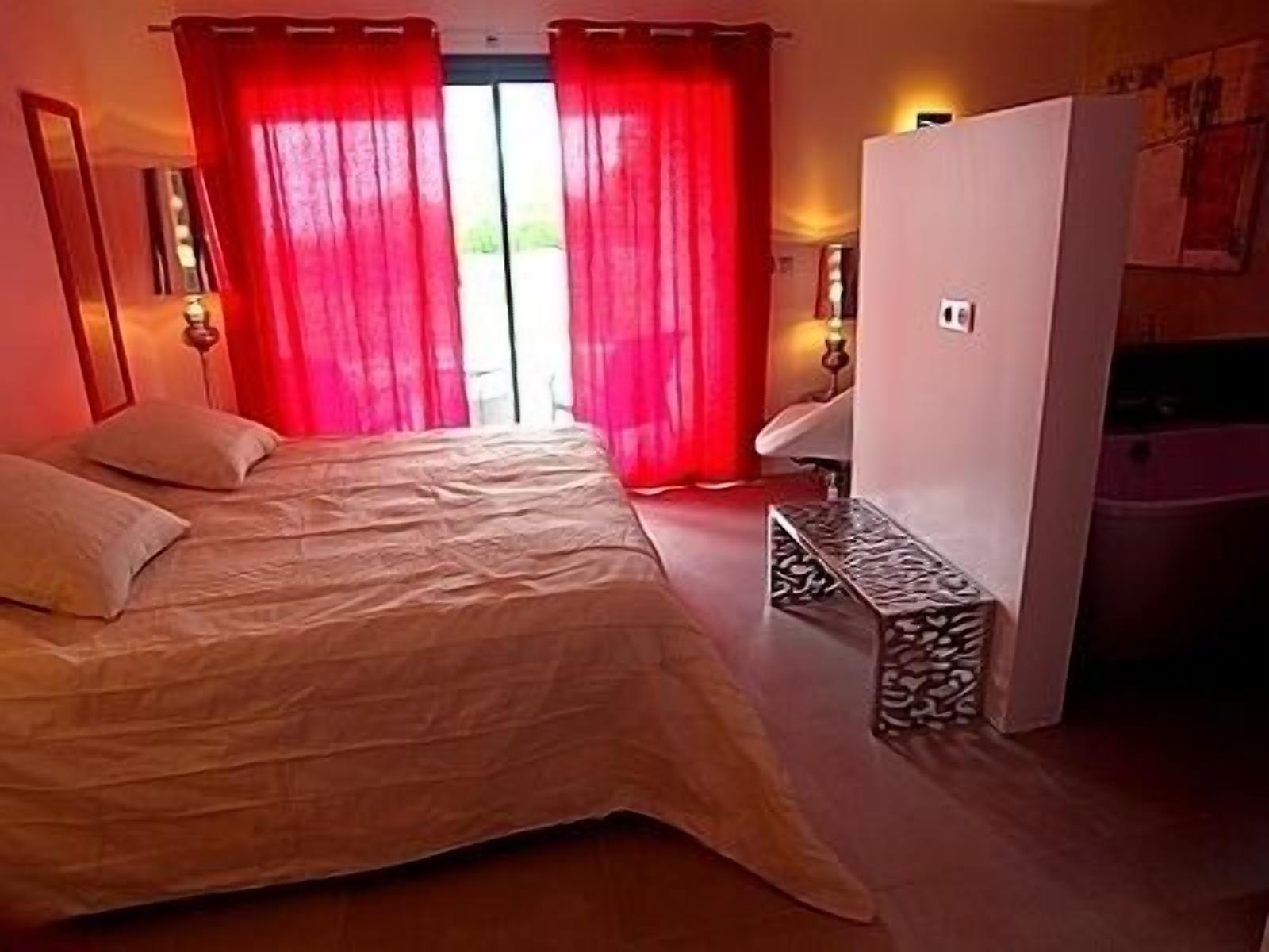 Un dormitorio con cama, una banca, un armario y una ventana con cortinas rojas.