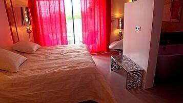 A bedroom with a bed, a bench, a wardrobe, and a window with red curtains.
