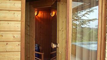 Una cabaña de madera con sauna, una terraza de madera y un ventanal de vidrio que da al exterior.