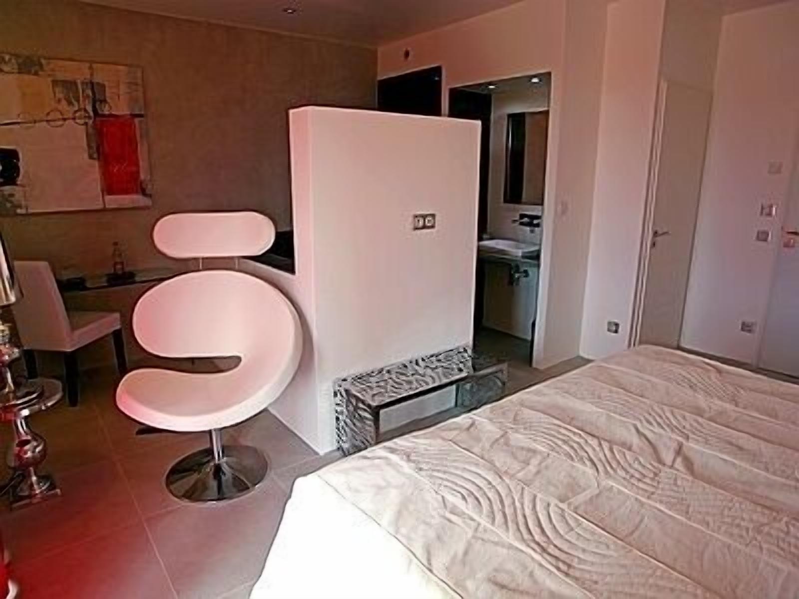 A modern hotel room with a large bed, a white chair, and a bathroom visible through an open door.