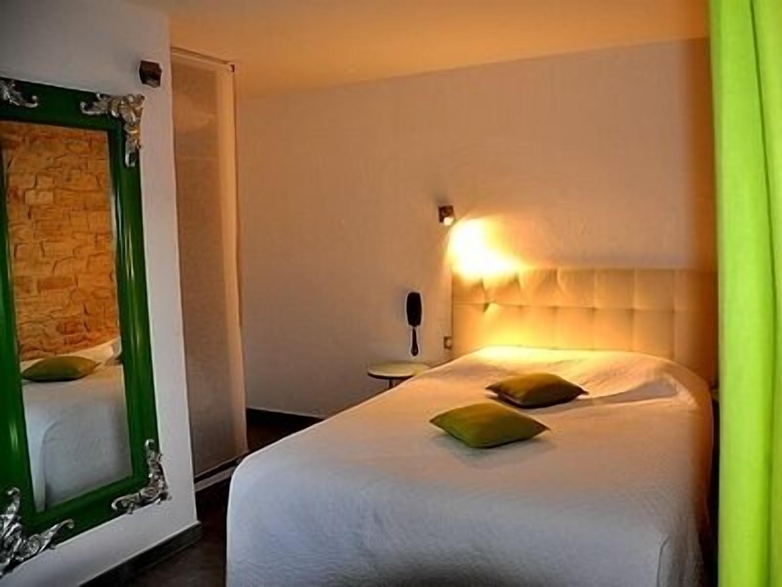 Una habitación de hotel con una cama grande, un espejo con marco verde y una lámpara fijada a la pared.