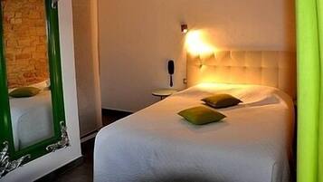 Una habitación de hotel con una cama grande, un espejo con marco verde y una lámpara fijada a la pared.