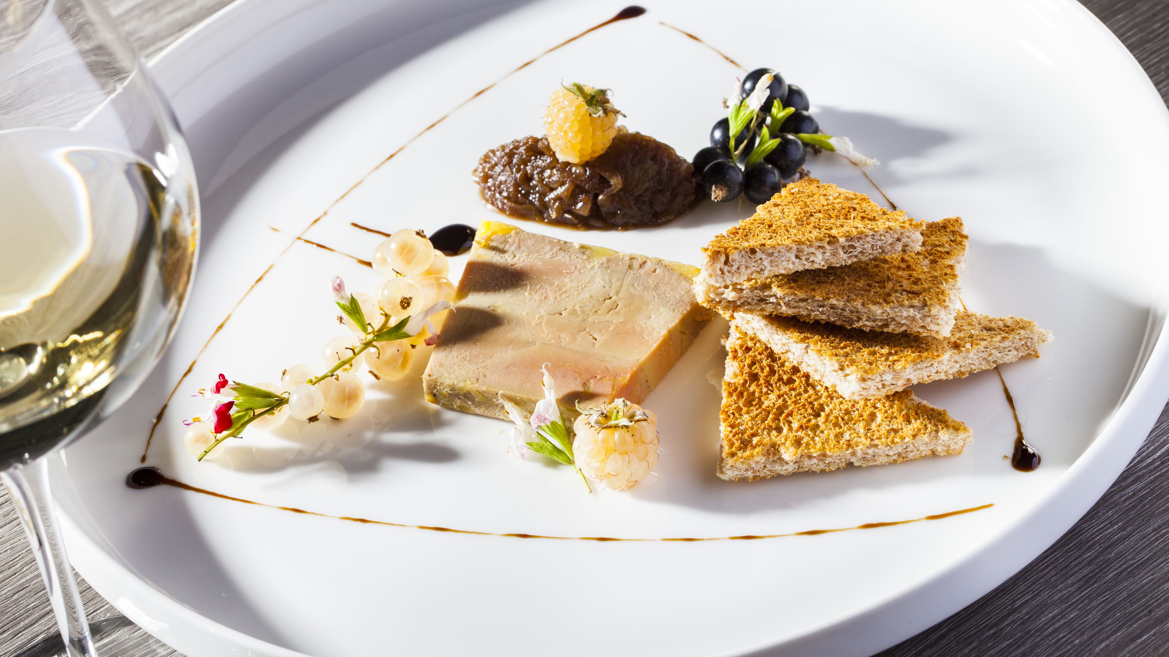 Un plato blanco con diversos alimentos, incluyendo un trozo de carne, pan, uvas y una pequeña fruta.