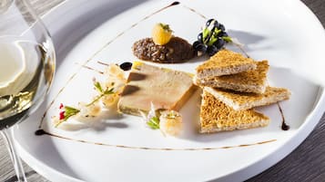 Een wit bord met diverse etenswaren, waaronder vlees, brood, druiven en een stukje fruit.