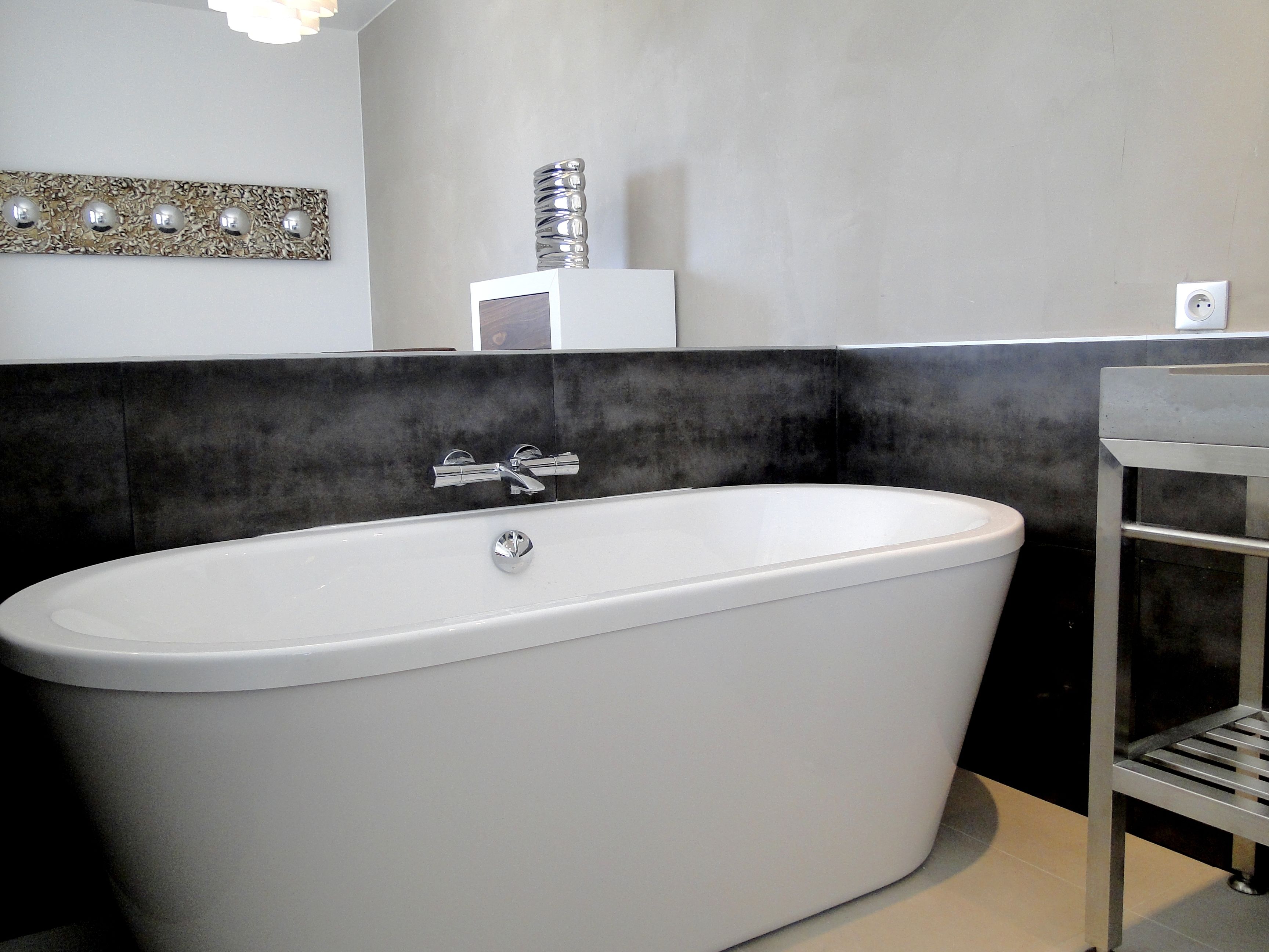 Une salle de bain moderne avec une baignoire sur pieds, un mur recouvert de carreaux noirs et blancs, et une étagère au design minimaliste.