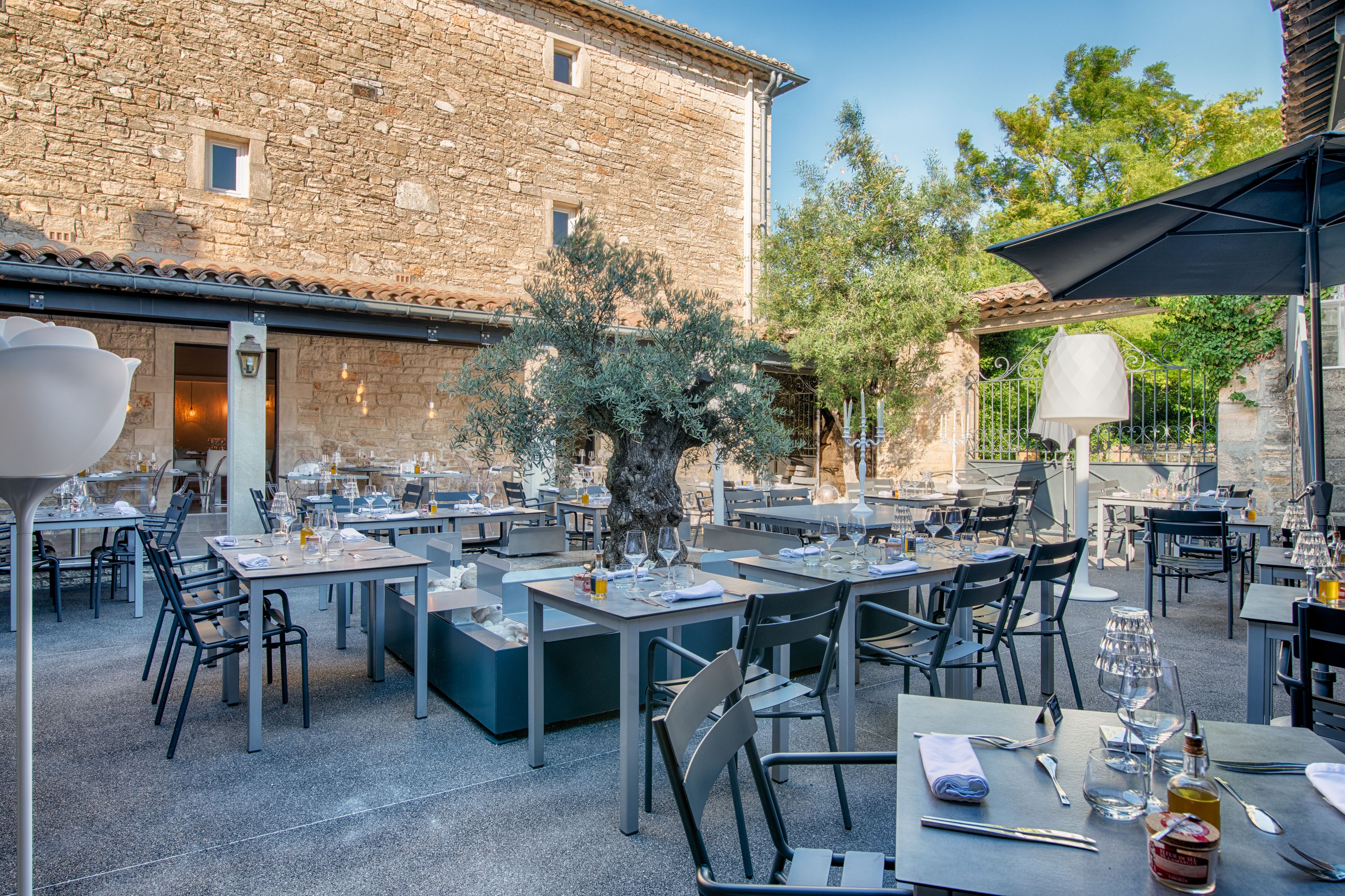 An outdoor dining area with stone walls, tables, chairs, and a tree.