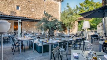 An outdoor dining area with stone walls, tables, chairs, and a tree.