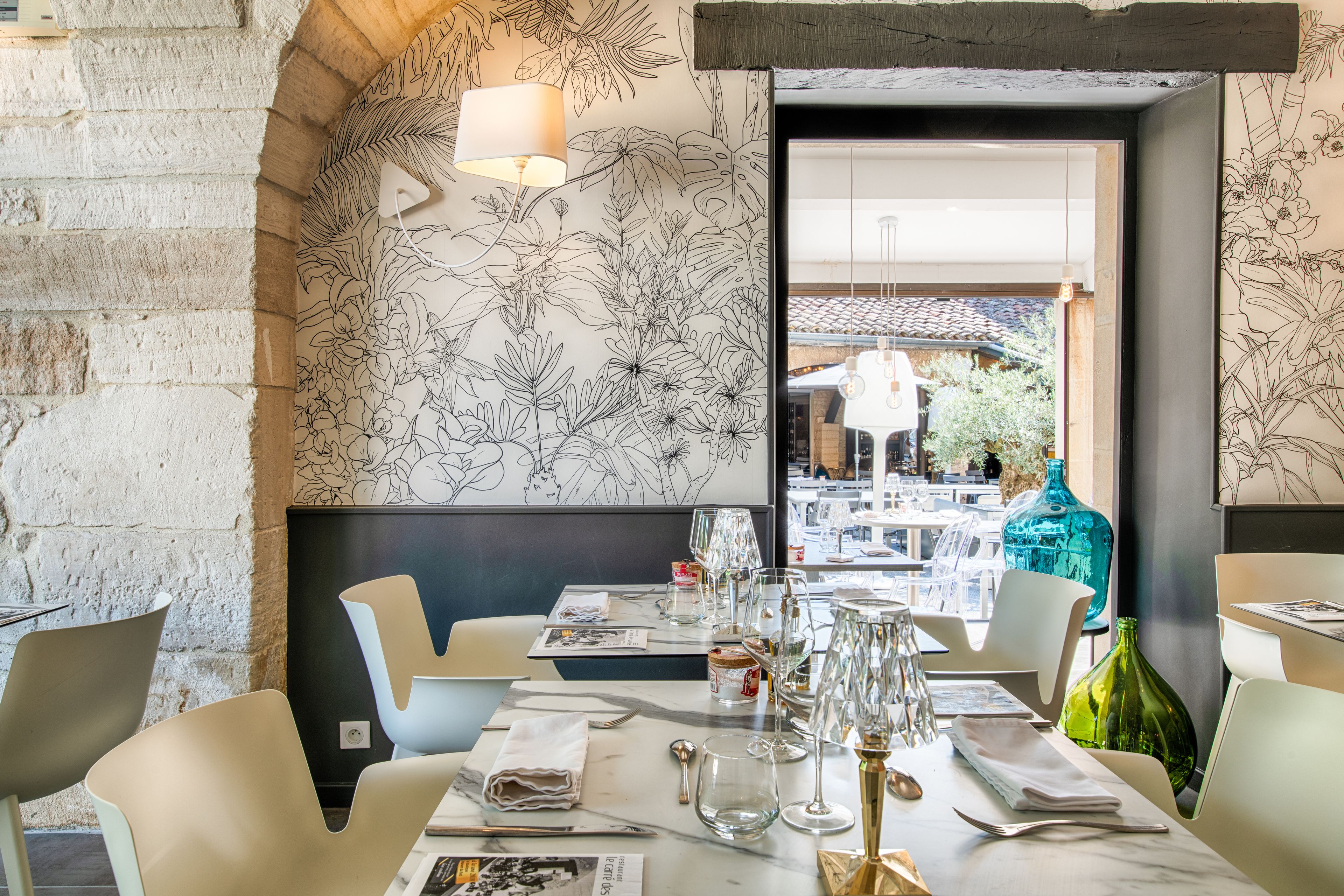 Un restaurant au décor moderne, avec un mur en briques, une fresque florale et une vue sur l’espace extérieur aménagé en terrasse.