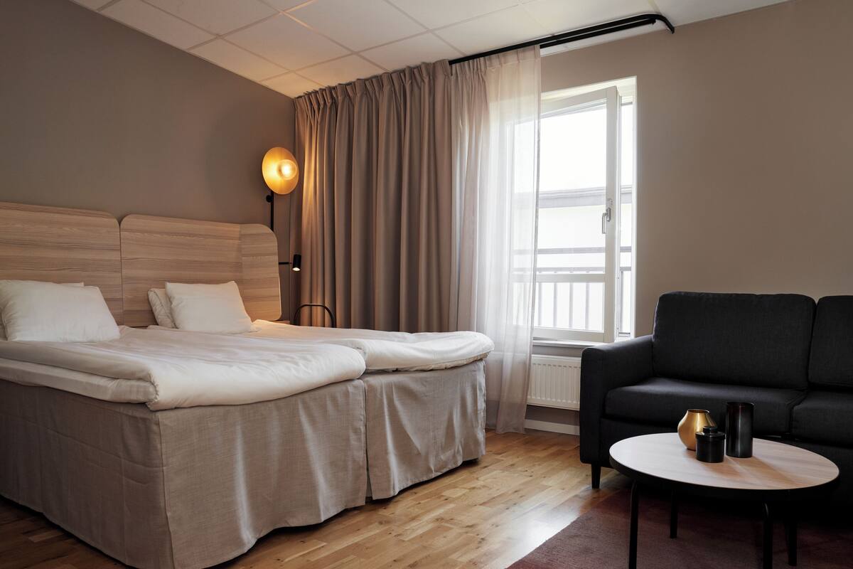 Ett hotellrum med en säng, en soffa, ett runt bord och en lampa.