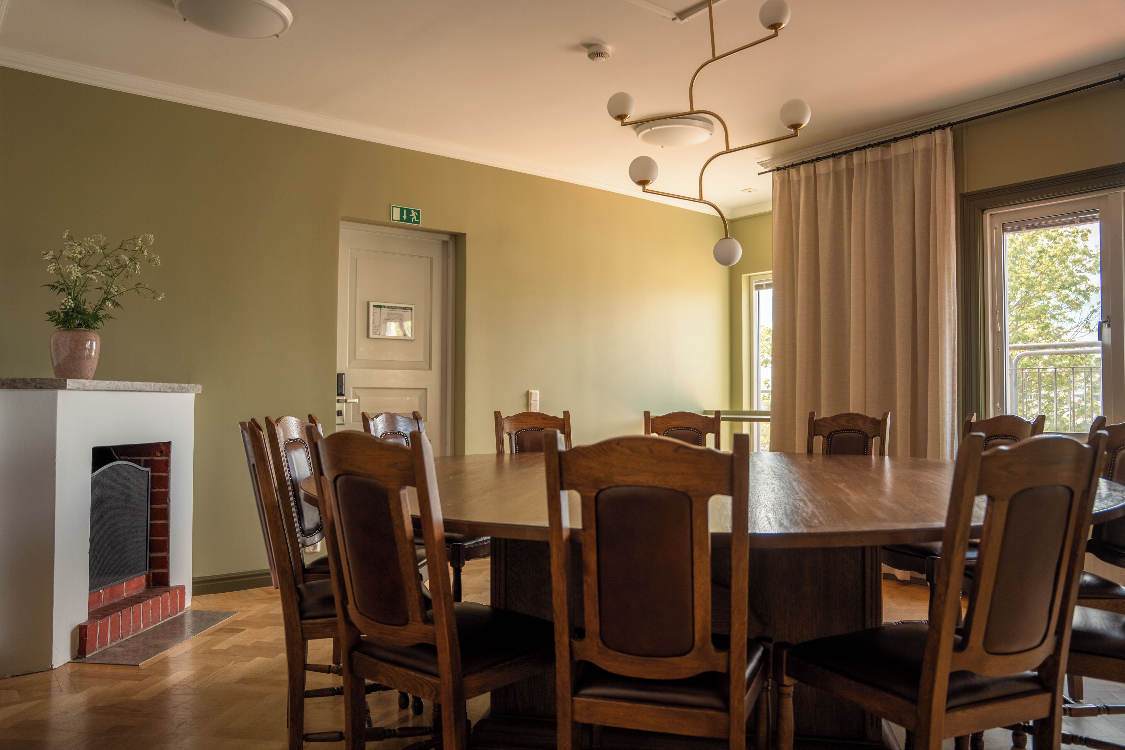 Un comedor con una gran mesa de madera y sillas, una chimenea y una puerta con letrero de salida.