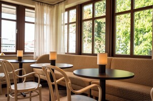 Un espace salon avec des tables et des chaises rondes, de grandes fenêtres avec des rideaux et une vue sur la verdure environnante.