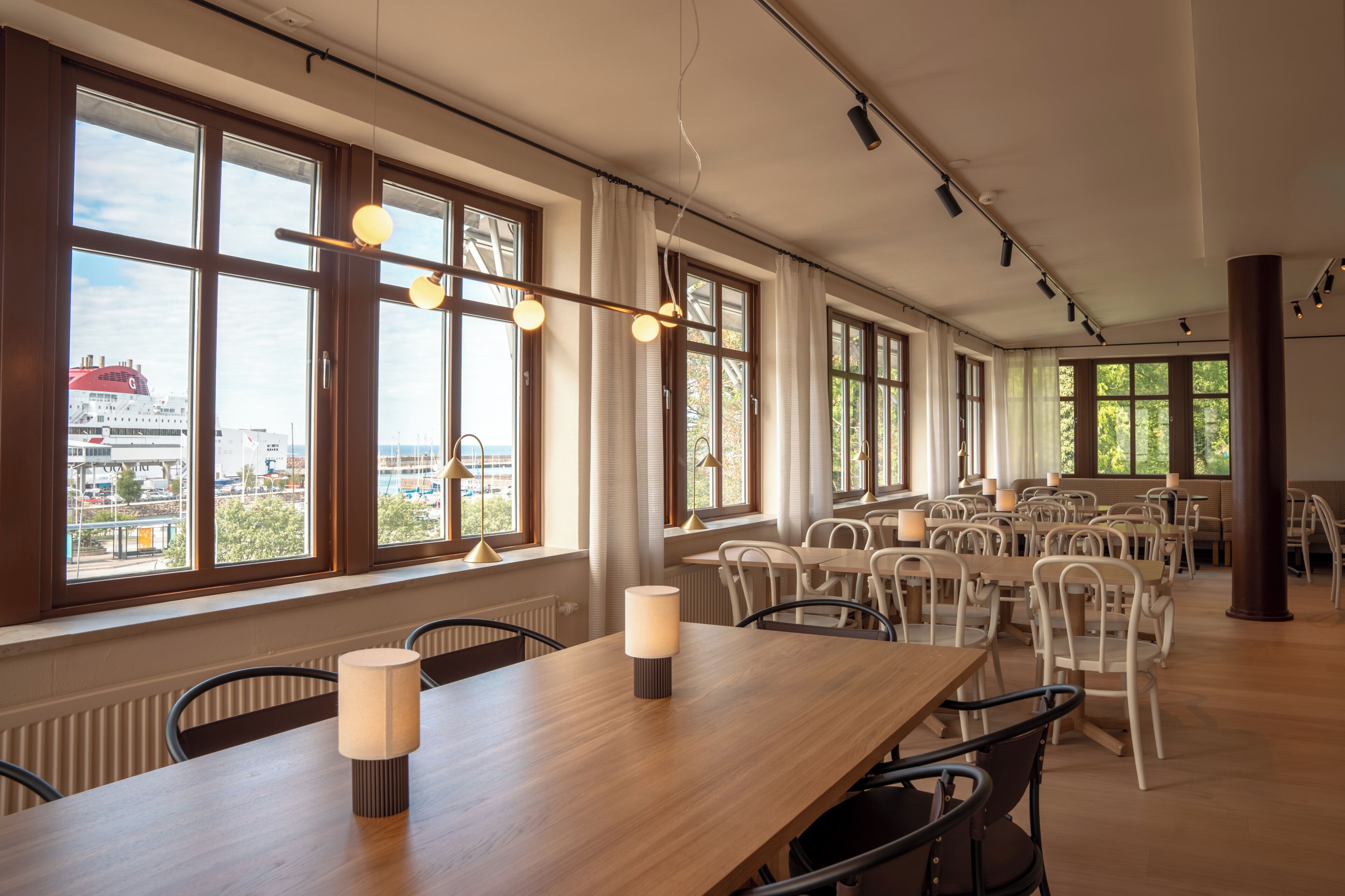 A spacious dining area with large windows, multiple tables, and chairs.