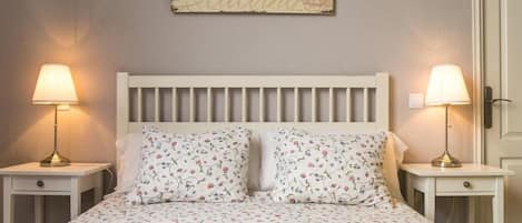 Un dormitorio con una cama blanca, ropa de cama floral, dos lámparas de noche y una cita motivadora en la pared.