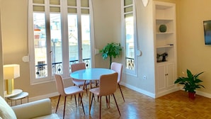 A dining area with a round table and four chairs, a potted plant, a television on a shelf, and a balcony with a view of buildings. - Hi Valencia Cánovas (Valencia)
