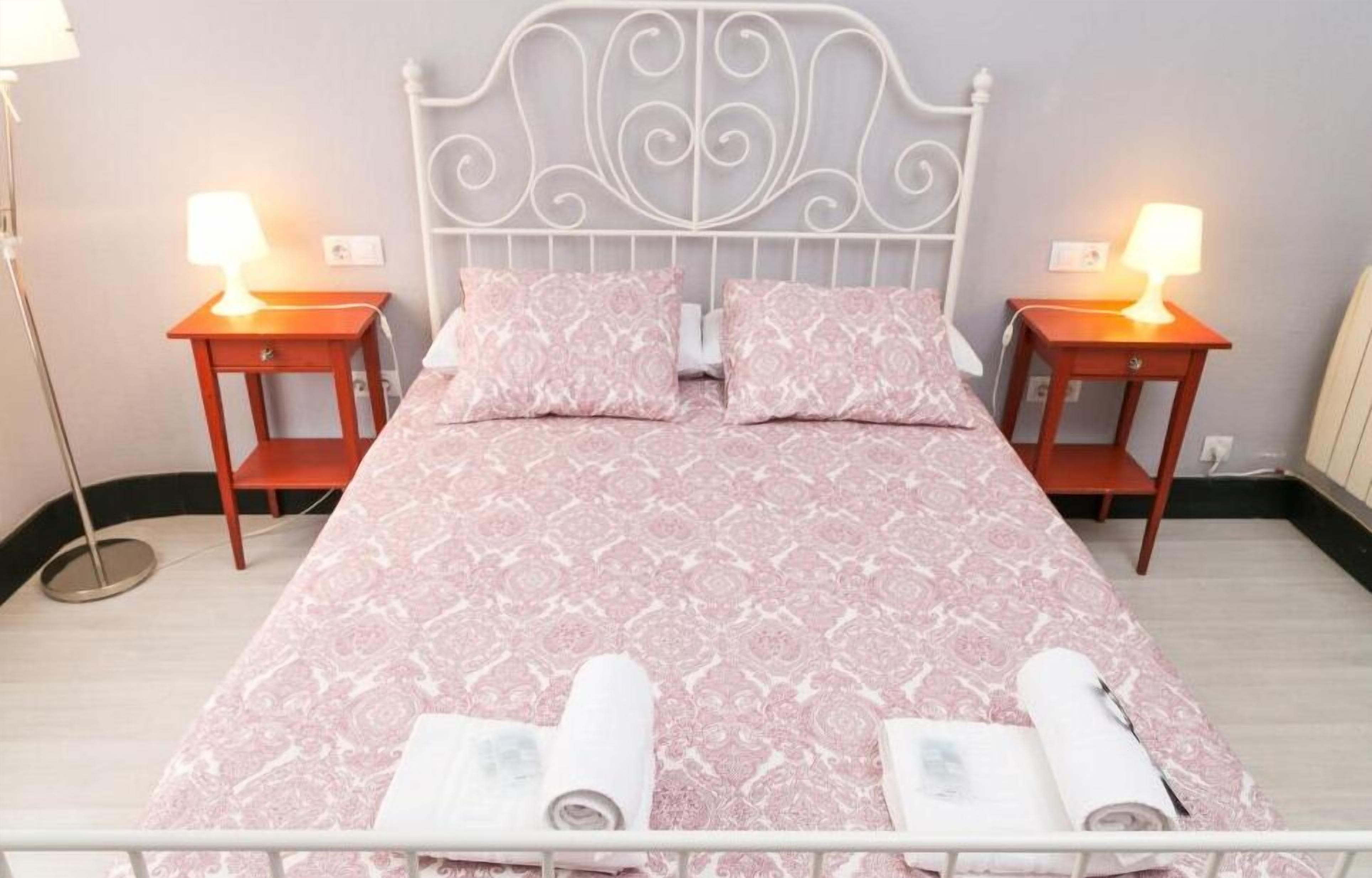 A neatly made bed with pink patterned bedding, two bedside tables with lamps, and a white metal headboard.