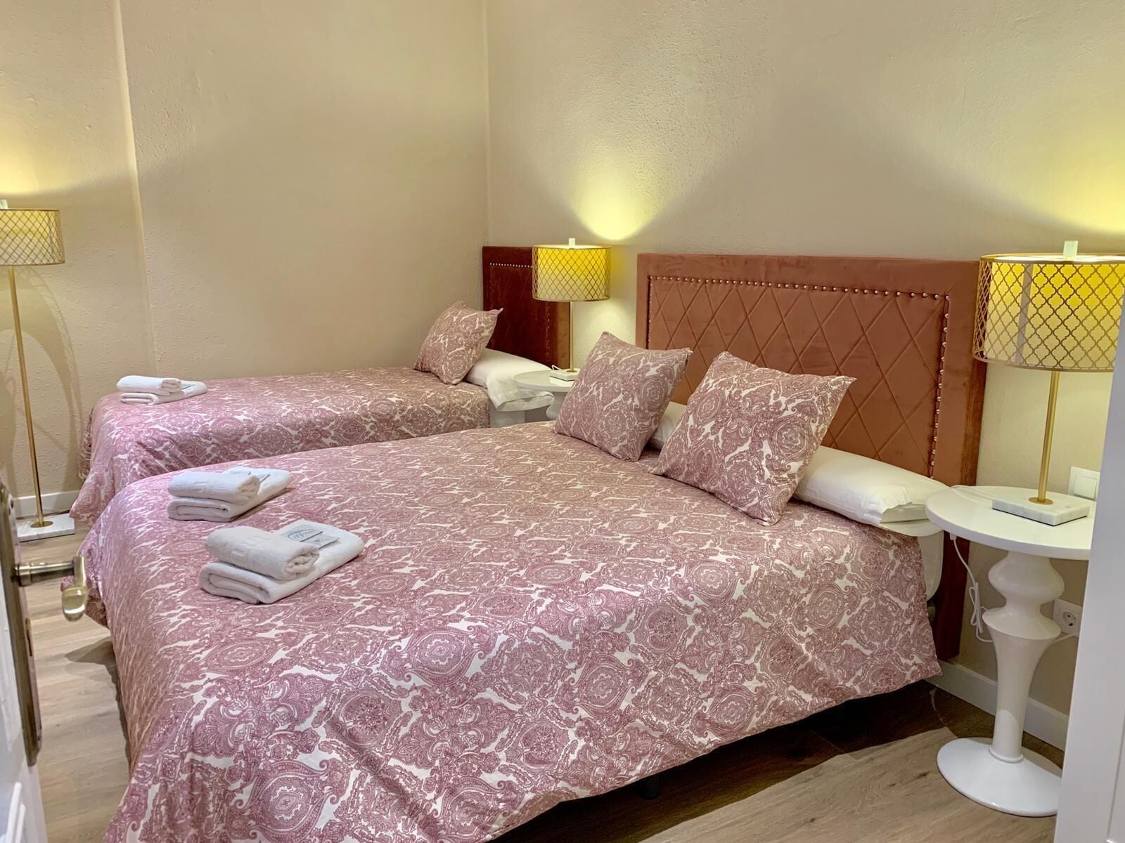 A hotel room with two beds, each with a headboard, bedside tables, and lamps.