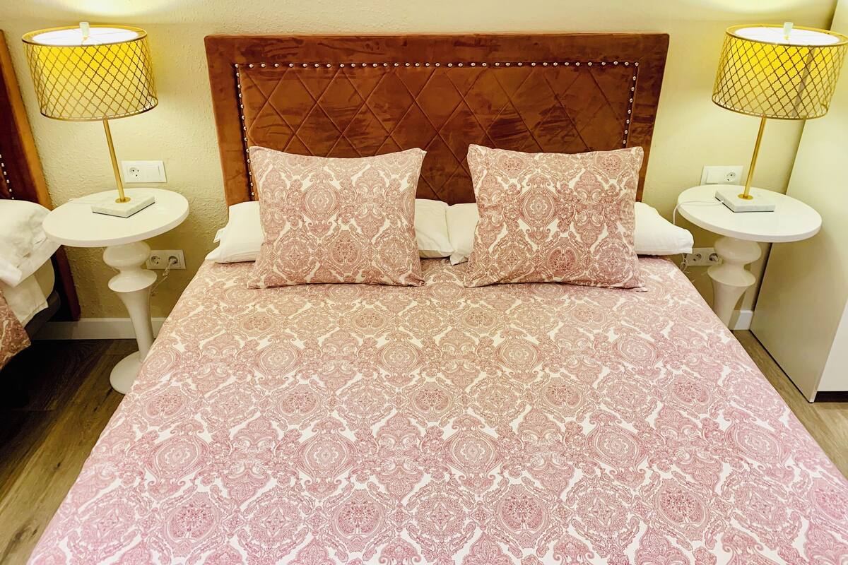 A neatly made bed with patterned bedding, two bedside lamps, and a headboard with a diamond pattern.